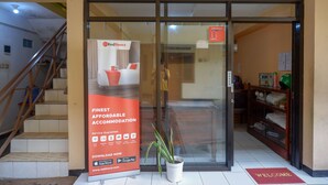 L’entrée d’un hôtel, avec une porte en verre, un escalier sur la gauche, un paillasson et une publicité pour RedDoorz.