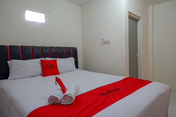 A neatly made bed with white linens, a red blanket, and a red pillow with a logo.