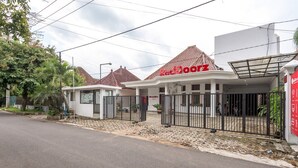 Un hôtel appelé « Red Door Inn », avec un toit recouvert de tuiles, une entrée fermée par un portail et une allée pavée.