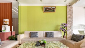Un salon avec un mur vert, un canapé beige, une table basse à motifs et une petite plante.