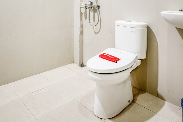 Un inodoro blanco con una caja de pañuelos rojos encima, un lavamanos blanco y un cabezal de ducha en la pared.