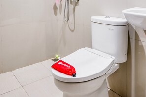 Des toilettes avec un sac rouge sur le couvercle, une pomme de douche et un accessoire de type bidet.