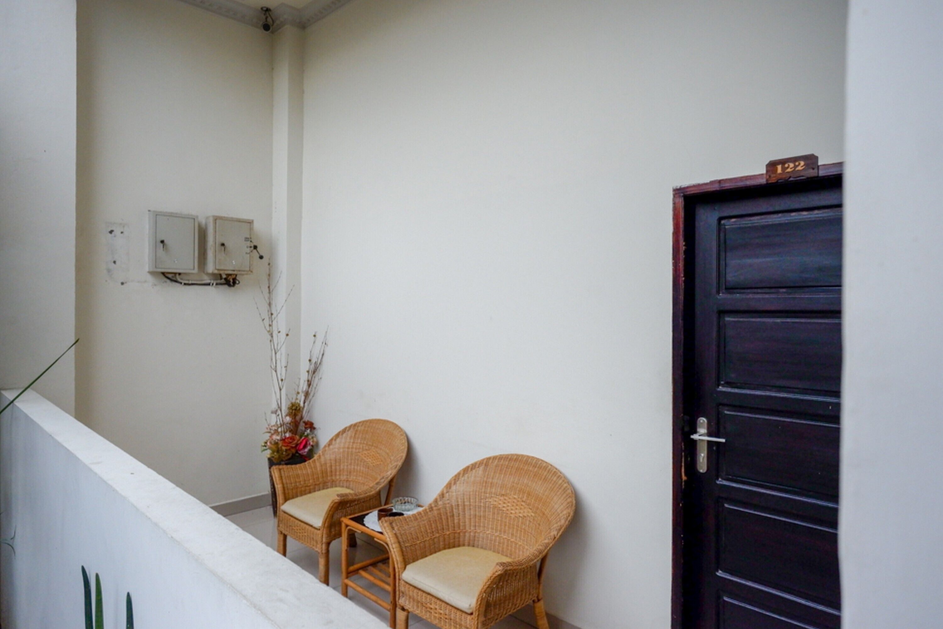 Un balcon avec deux fauteuils en osier, une porte en bois foncé et un petit numéro de porte.