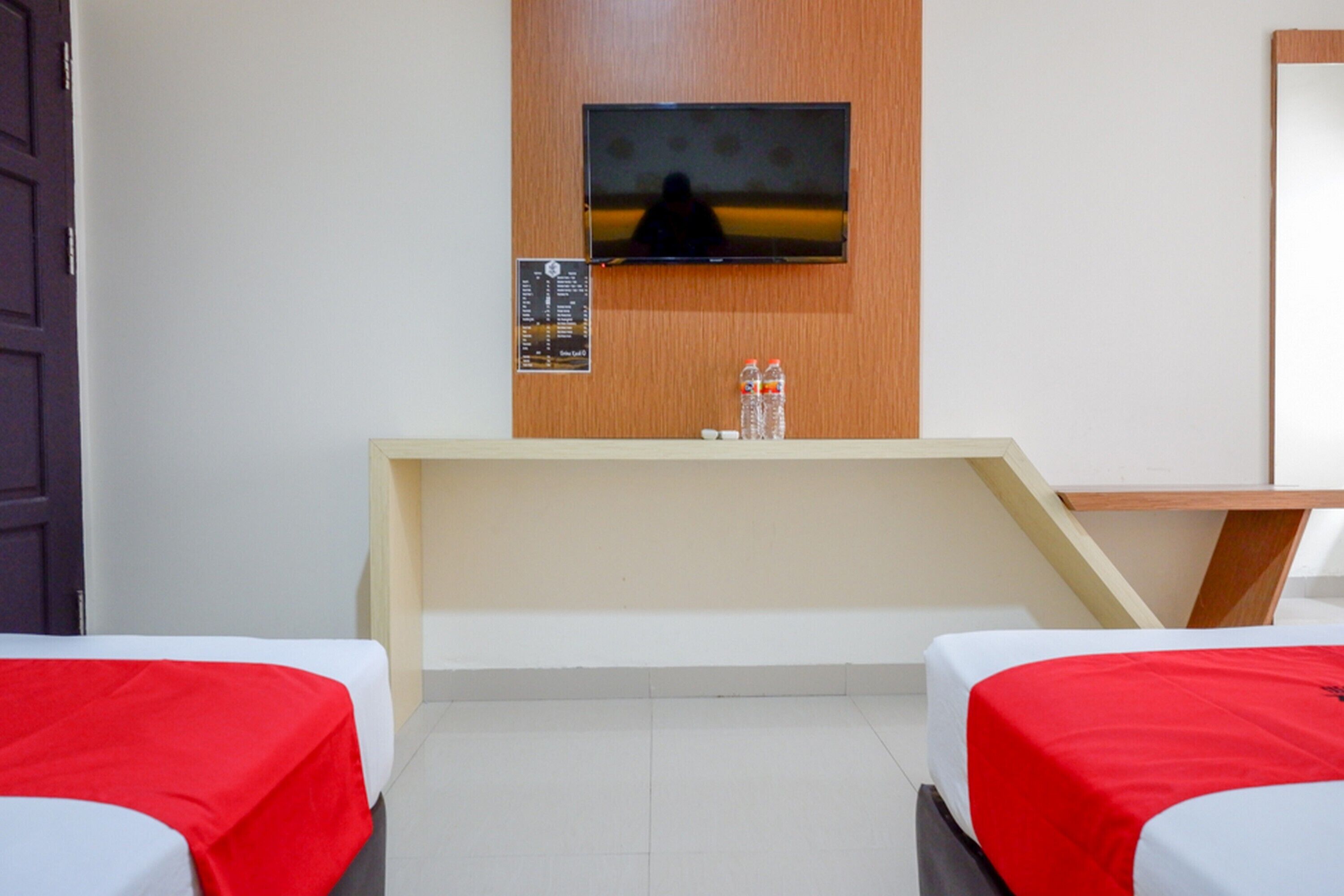 A hotel room with two beds, a TV mounted on the wall, and a small table with two bottles of water.