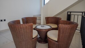 A wicker dining set with cushioned seats and a central table, positioned in a bright room with a staircase and a railing. - RedDoorz @ Hotel Bumi Palupy (Palu)