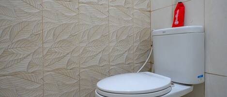 A white toilet with a red cleaning bag on top, set against a wall with a leaf pattern.