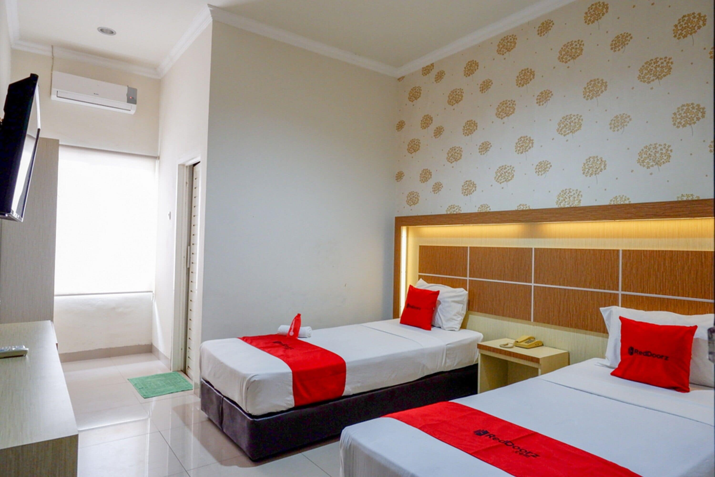 A hotel room with two beds, a TV, an air conditioner, and a patterned wall.