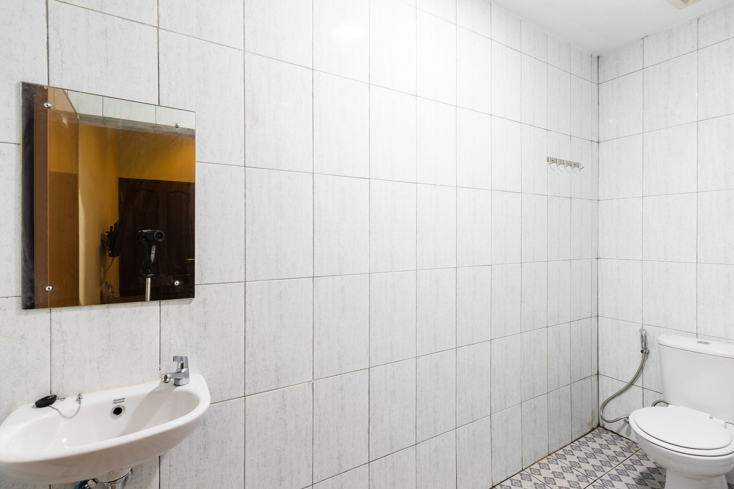 A bathroom with white tiles, a sink, a mirror, and a toilet.