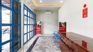 A reception area with a reception desk, blue chairs, a patterned floor, and a wall-mounted air conditioner. - RedDoorz near Medan Amplas (Medan)
