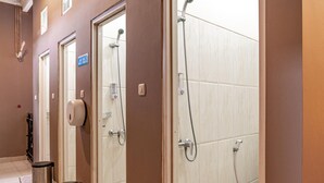Une salle de bain d’hôtel équipée de plusieurs douches, de sèche-mains et de poubelles.