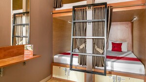 Une chambre avec un lit superposé, une échelle, une étagère avec une pancarte et un oreiller rouge sur le lit.