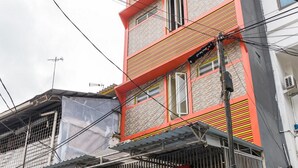 Un bâtiment arborant une enseigne RedDoorz, avec une façade rouge et orange, de nombreuses fenêtres et des câbles électriques apparents.