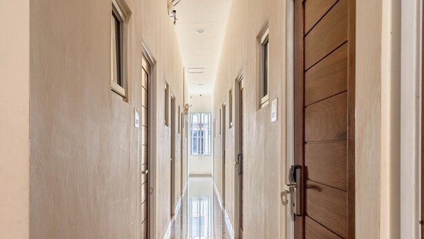 Un long couloir étroit, avec des portes de part et d’autre, qui mène à une pièce lumineuse au bout.