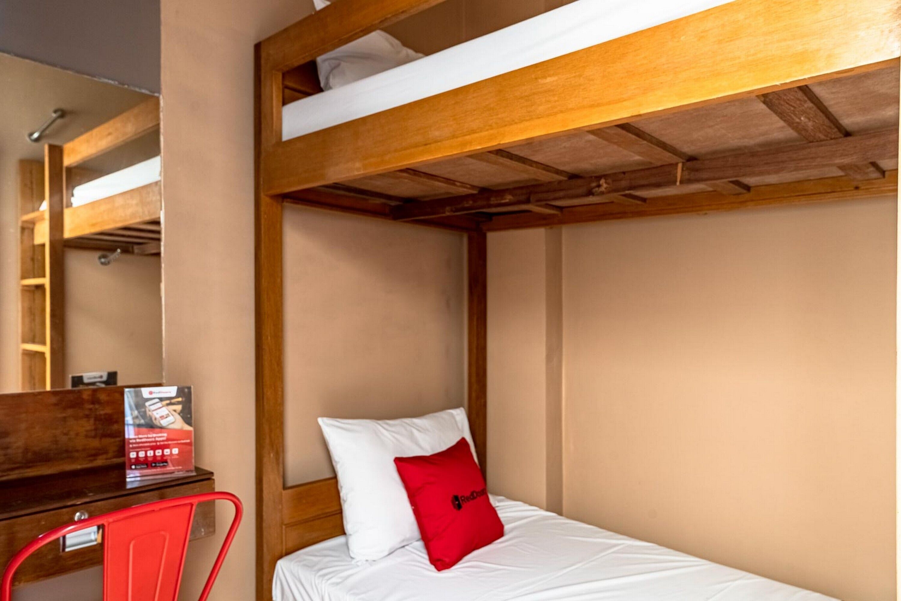 Una cama litera con estructura de madera, un escritorio con una silla y una almohada roja en la cama.