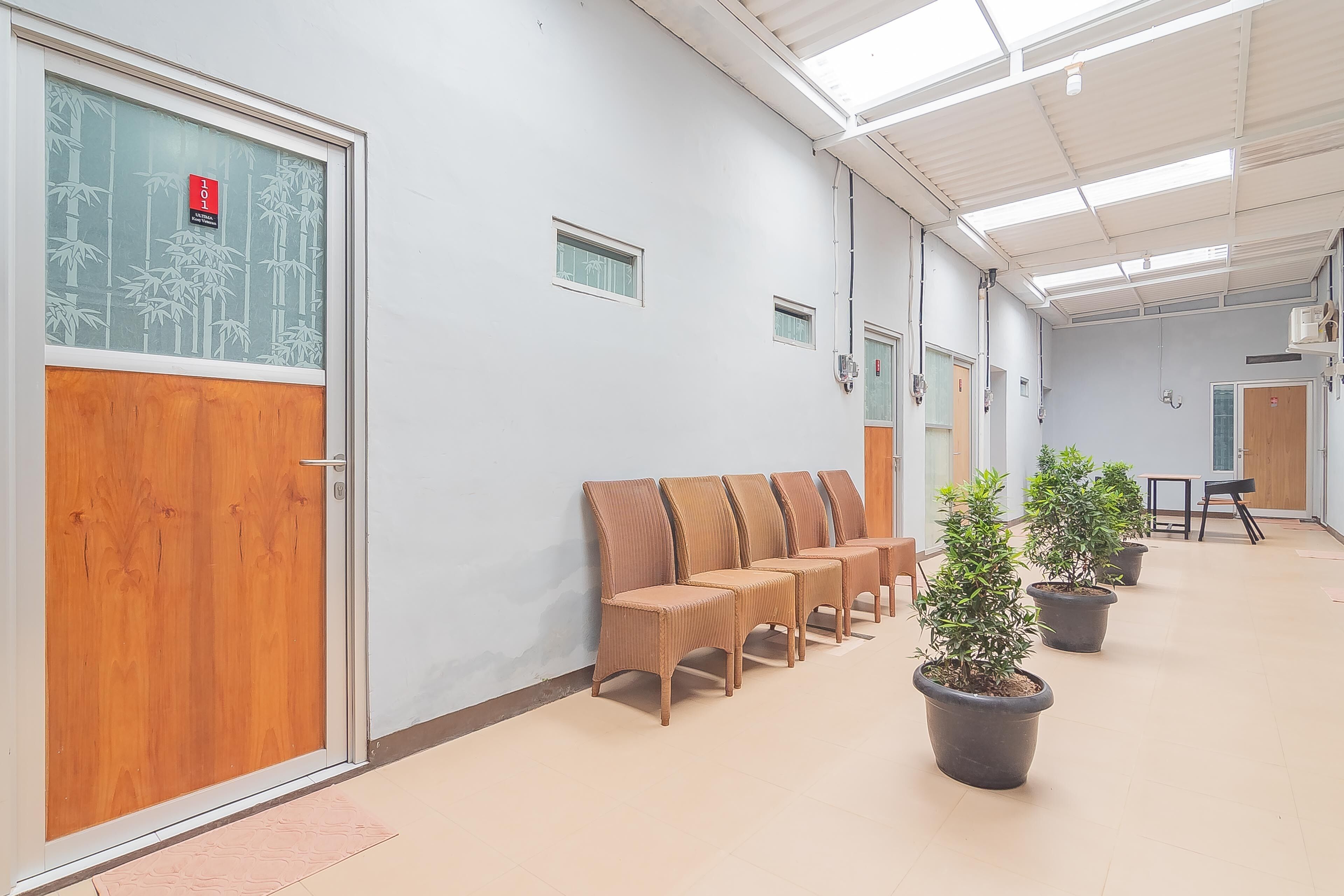 A hallway with wooden doors, a row of chairs, and potted plants.