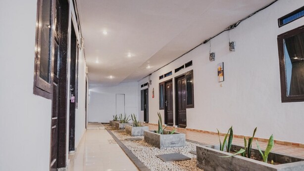 A corridor with a tiled floor, concrete planters with plants, and doors with dark frames. - RedDoorz near Jalan Soeprapto Bengkulu (Bengkulu)