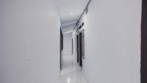 A narrow, white-walled hallway with tiled flooring and doors on one side. - RedDoorz near Jalan Soeprapto Bengkulu (Bengkulu)