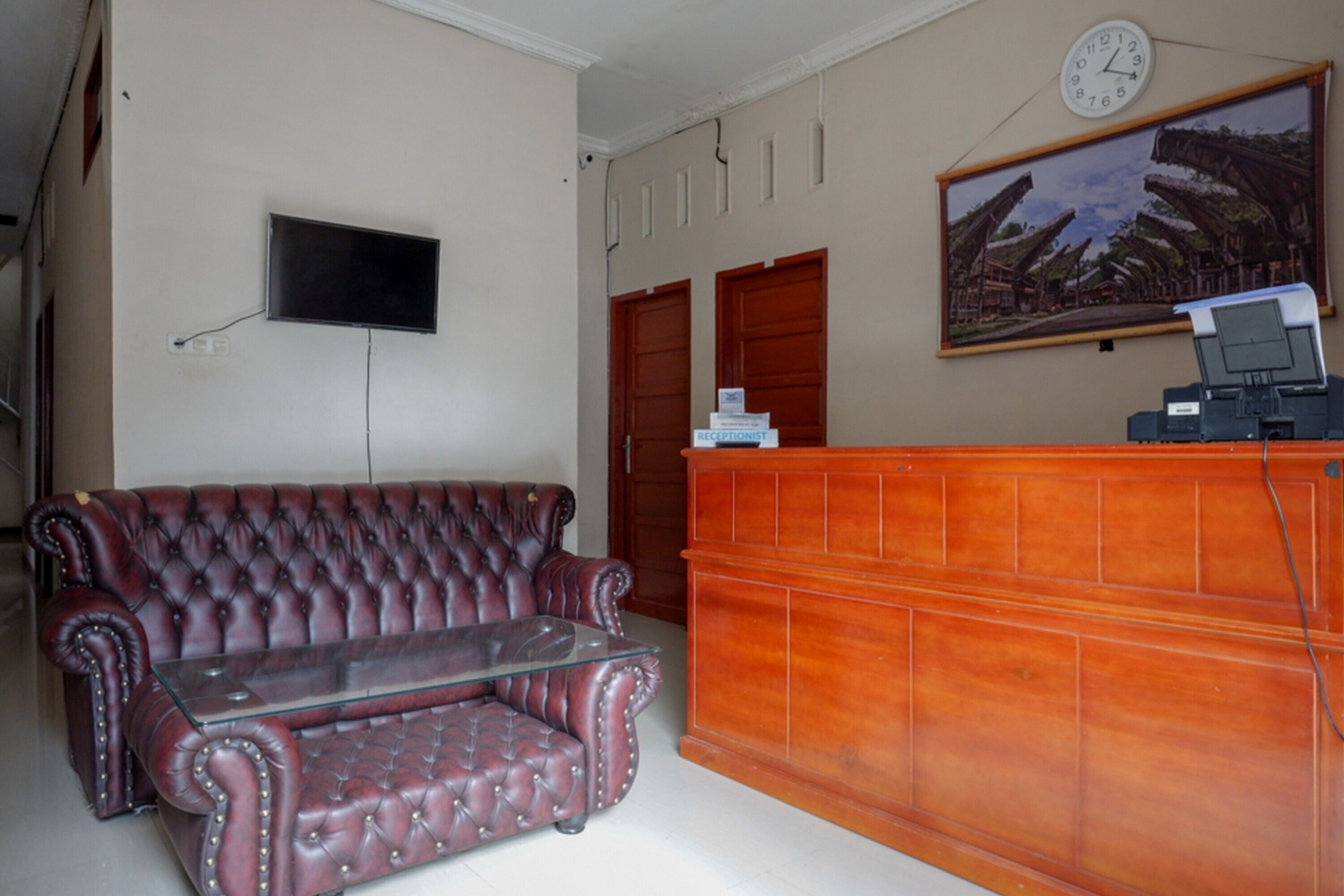 Un espace d’accueil comprenant un bureau en bois, un canapé en cuir, une table basse en verre, un téléviseur à écran plat fixé au mur et un tableau au-dessus du bureau.