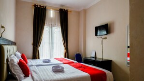 Une chambre d’hôtel avec un lit, un bureau, une télévision et une fenêtre avec des rideaux.