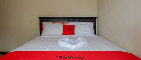 A neatly made bed with a red and white bedspread, a heart-shaped towel, and a pillow with the RedDoorz logo.