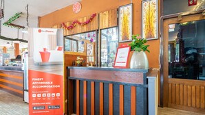 Een receptiebalie met een RedDoorz bord, een poster met een servicegarantie en een plant.