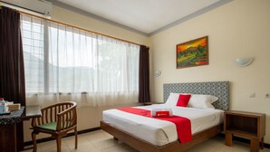 Een hotelkamer met een bed, een bureau, een stoel, een nachtkastje en een schilderij aan de muur.