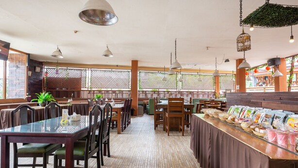 Een restaurant met meerdere tafels en stoelen, een toonbank met etenswaren en hangende lampen.