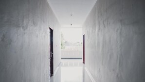 A corridor with a reflective floor and plain walls, leading to an open area with a view of the outside. - RedDoorz Syariah near Balai Kota Bengkulu (Bengkulu)