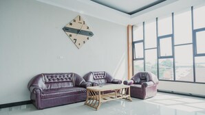 A modern living room with a purple leather sofa, a wooden coffee table, and a wall clock. - RedDoorz Syariah near Balai Kota Bengkulu (Bengkulu)