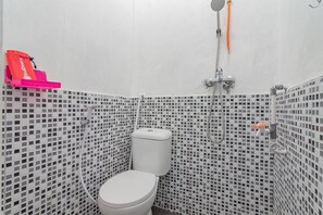 Un baño con inodoro, ducha y una pequeña estantería con un bolso rojo.