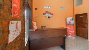 A reception desk with a brick wall and RedDoorz signage, a wooden door labeled "STAFF ONLY", and a RedDoorz advertisement.