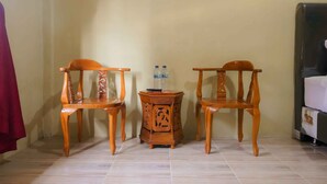 A room with two wooden chairs, a small wooden table with two bottles, and a bed with a white cover.