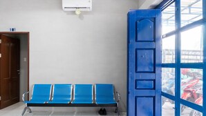Un área de espera con un banco, un equipo de aire acondicionado y una puerta azul que da al exterior.