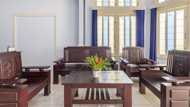A room with wooden furniture, a central table with a potted plant, and large windows with blue curtains.