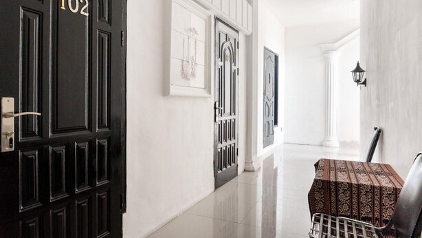 A hallway with a black door labeled "102," white walls, and a tiled floor. - RedDoorz near Manhattan Times Square Medan 2 (Medan)