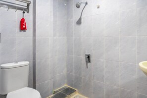 A bathroom with grey tiles, a white toilet, a shower, and a red bag hanging on the wall.