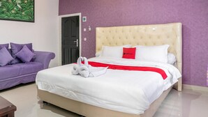 A hotel room with a large bed, a purple sofa, and a door. - RedDoorz near Manhattan Times Square Medan 2 (Medan)