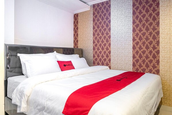 A hotel room with a bed, white bedding, a red throw, and patterned wallpaper.