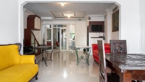 A living room with a yellow sofa, a dining table, and a red chair. There is a staircase leading to another room. - RedDoorz near Manhattan Times Square Medan 2 (Medan)