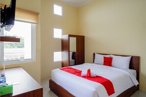 A hotel room with a bed, a desk, a wardrobe, and a window with blinds. - RedDoorz near Graha Saba Buana Solo (Colomadu)