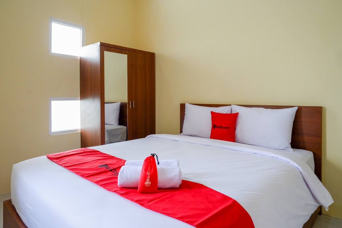 A hotel room with a neatly made bed, a wooden wardrobe, and a small window.