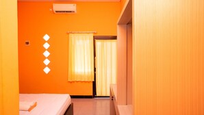 A hotel room with an orange wall, a bed, a window with curtains, and an air conditioning unit. - KoolKost Syariah near Transmart Tegal (Tegal)