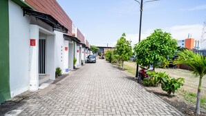 A paved walkway between buildings with a parked car and a motorcycle. - KoolKost Syariah near Transmart Tegal (Tegal)