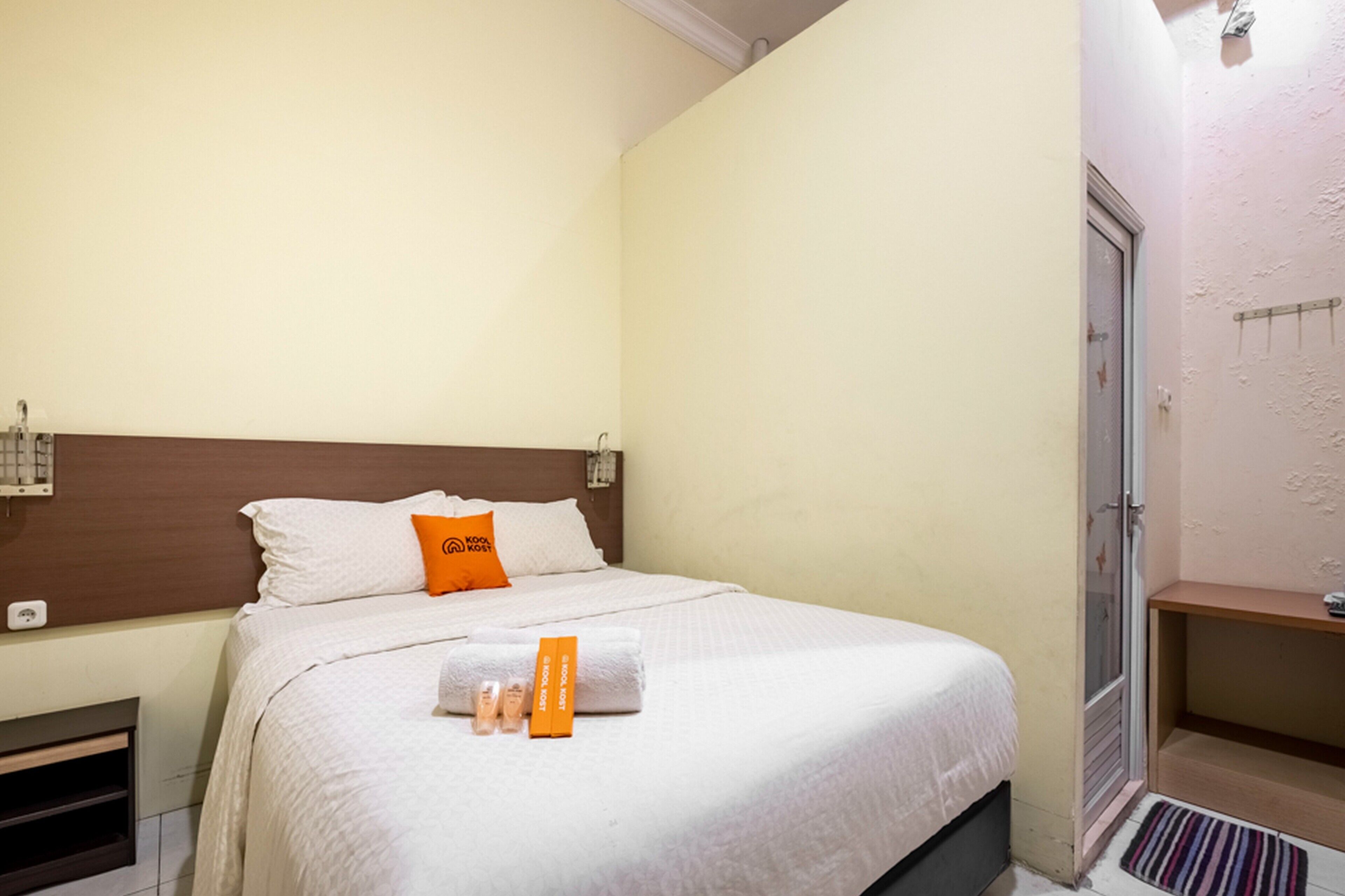 Een net opgemaakt bed met witte lakens, een oranje kussen en toiletartikelen op het bed.