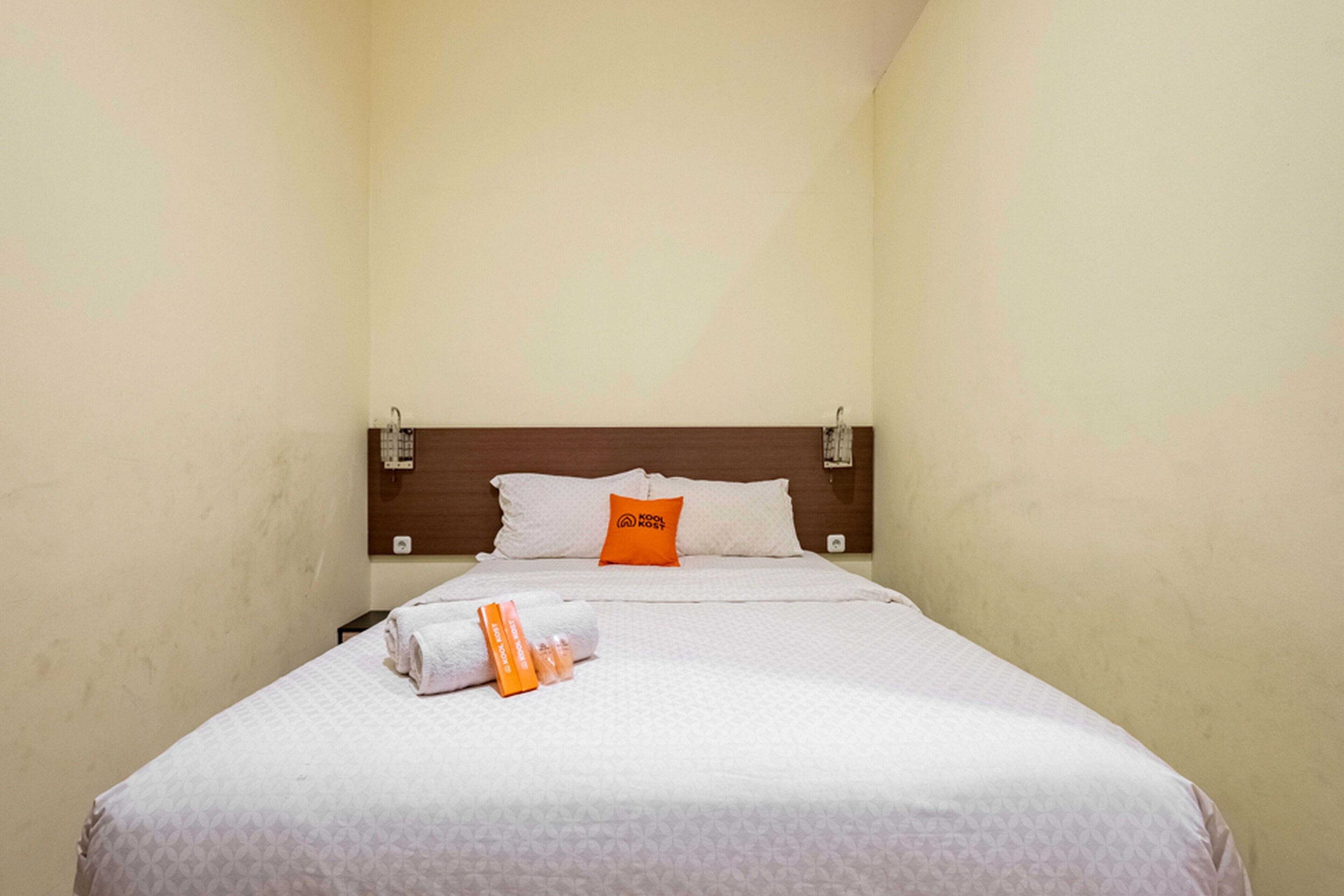 Una habitación de hotel con una cama, un cabecero de madera, una pared blanca y una mesita de noche con una lámpara.