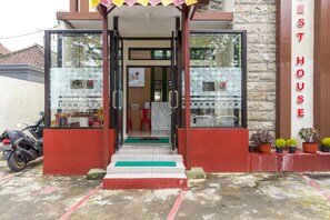 Entrada d'un hotel amb façana de vidre, una moto aparcada a l'exterior i plantes en testos a la dreta.