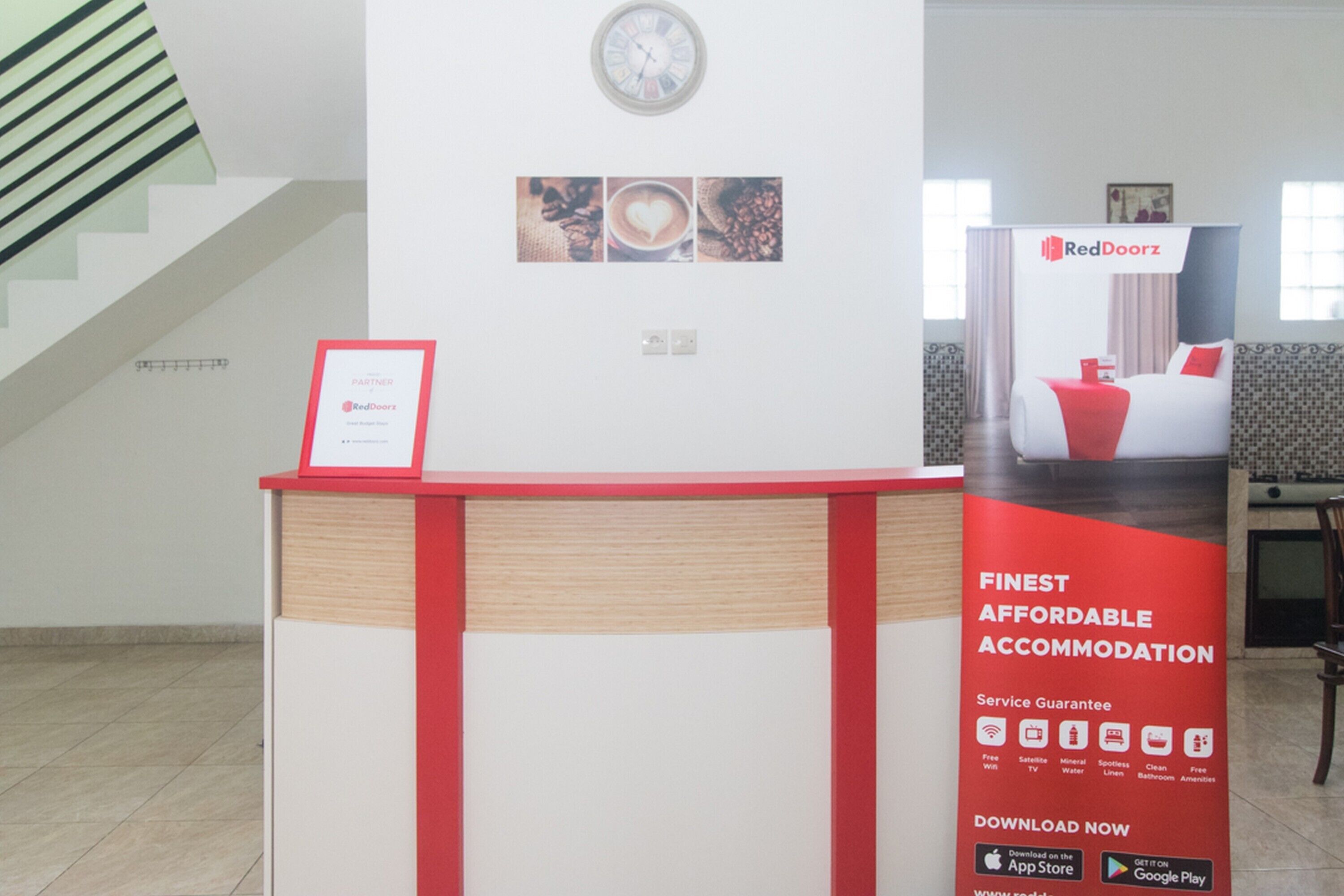 A hotel reception desk with a RedDoorz sign, a clock, and a service guarantee poster.