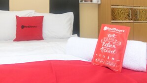 Ein Hotelzimmer mit einem Bett, einem roten Kopfkissen und einem Artikel der Marke RedDoorz auf dem Bett.