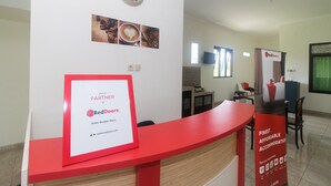Ein Empfangsschalter mit einem RedDoorz-Schild, einer Uhr und gerahmten Bildern mit Kaffeemotiven an der Wand.