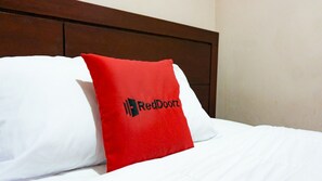 A bed with white bedding and a red pillow with the RedDoorz logo. - RedDoorz @ Jalan Cendrawasih Timika (Timika)